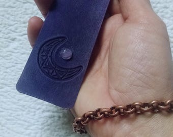 May include: A purple leather bookmark with a crescent moon design and a small pink stone in the center. The bookmark has the word "chadia" embossed on it.