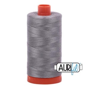 Puede incluir: Una bobina de hilo gris con una bobina de plástico roja y naranja. El hilo está etiquetado con "AURIfil".