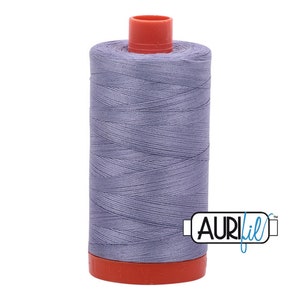 Pode incluir: Uma bobina de fio de cor roxo claro com uma bobina de plástico vermelha e o texto "Aurifil" sobre um fundo branco.