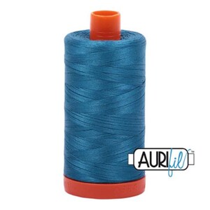 Op de afbeelding: Een spoel tealblauwe draad met een oranje plastic spoel en de tekst "AURIfil" aan de zijkant.