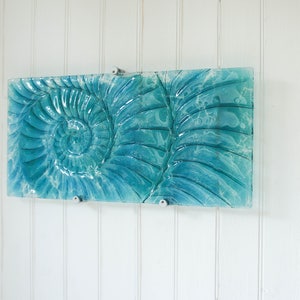 May include: A teal blue glass wall art piece featuring a raised, textured design of a nautilus shell.