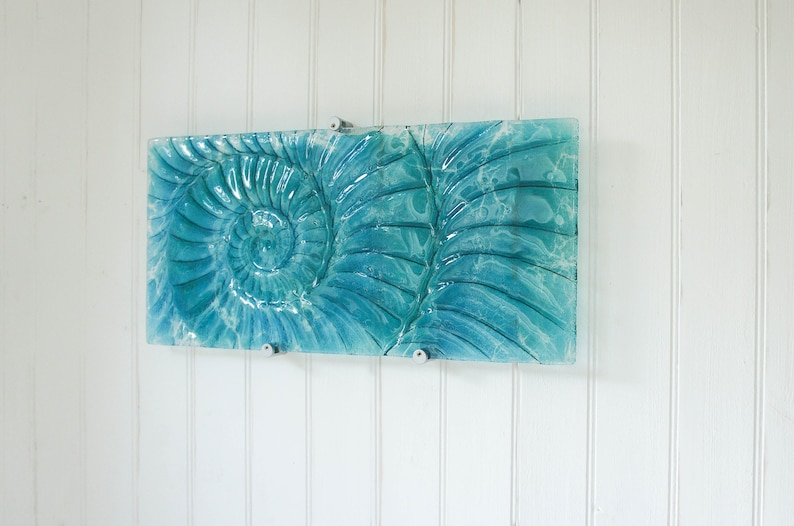 May include: A teal blue glass wall art piece featuring a raised, textured design of a nautilus shell.