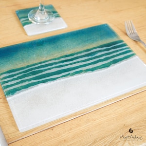 May include: A blue and white glass placemat with a design of waves and sand. The placemat is made by Matt Adkins Glass.