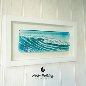 May include: A framed glass relief sculpture of a blue ocean wave with white foam. The sculpture is titled "Matt Adkins Glass Relief".