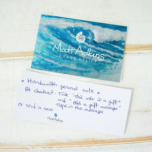 May include: A handwritten note on a white card with blue text. The note says "*Handwritten personal note* At checkout: Tick "This order is a gift" and add a gift message. Type in the message or send a card. Matt Adkins".