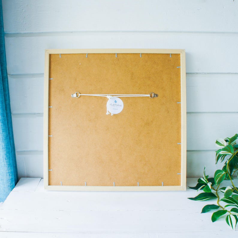 May include: The back of a framed print with a white frame and a brown backing. A white tag with the text "Handmade" is attached to the backing.