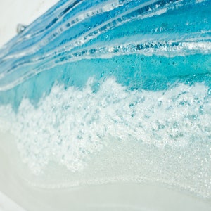 Puede incluir: Primer plano de una pieza de arte de vidrio azul y blanco que representa olas del oc&eacute;ano. La pieza est&aacute; hecha con capas de vidrio, creando un aspecto realista y texturizado.