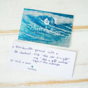 May include: A rectangular business card with a blue and white abstract wave pattern, a white shell icon, and the text Matt Adkins GLASS RELIEF. Below it, a white card with blue handwritten text explaining how to add a gift message at checkout.