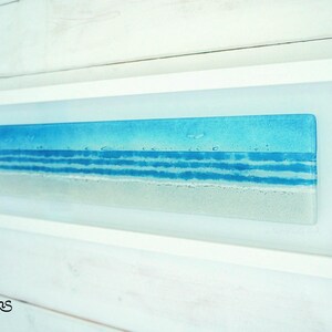 panoramic 3D fused glass blue beach scene wall art in a white wooden frame with cord across the back, ready to hang 60x20cm with cable across the back, handmade by glass artis Matt Adkins in Dorset, UK