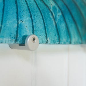 May include: Close-up of a silver wall mount with a screw visible. The mount is attached to a piece of blue glass art.