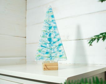 Puede incluir: Un adorno de árbol de Navidad de vidrio azul y blanco con una base de madera. El árbol está decorado con un diseño moteado blanco y azul.
