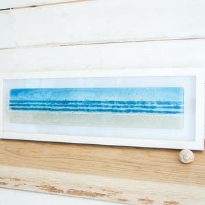 panoramic 3D fused glass blue beach scene wall art in a white wooden frame with cord across the back, ready to hang 60x20cm with cable across the back, handmade by glass artis Matt Adkins in Dorset, UK