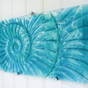 May include: A rectangular piece of glass art with a blue and white swirl pattern. The pattern resembles a nautilus shell.