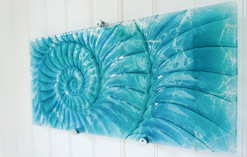 May include: A rectangular piece of glass art with a blue and white swirl pattern. The pattern resembles a nautilus shell.