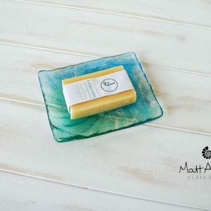 May include: A bar of citrus zing handmade soap on a blue and green glass soap dish. The soap is wrapped in white paper with the text "Citrus Zing Handmade Soap" printed on it.