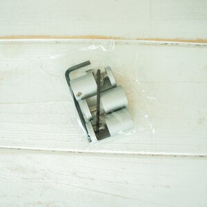 May include: A package containing three silver metal shelf brackets and a small black tool. The brackets are in a clear plastic bag.
