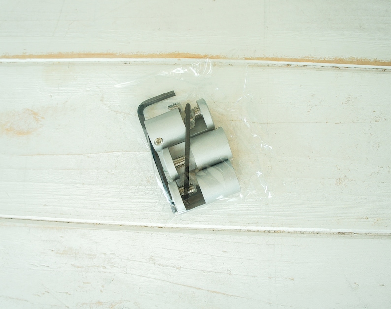 May include: A package containing three silver metal shelf brackets and a small black tool. The brackets are in a clear plastic bag.
