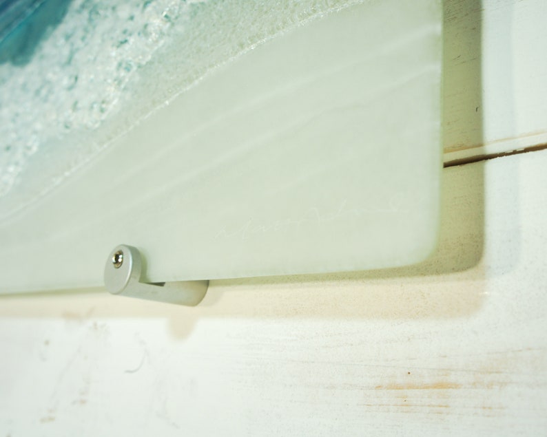 Puede incluir: Primer plano de un soporte de pared de metal plateado fijado a un panel de vidrio esmerilado. El soporte tiene un peque&ntilde;o tornillo en el lateral.