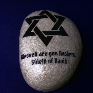 May include: A gray stone with a black Star of David and the text "Blessed are you Hashem, Shield of David" painted on it.