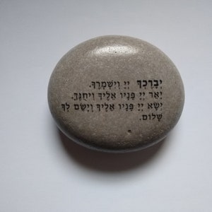 May include: A gray stone with Hebrew text inscribed on it. The text reads: "May you be blessed and protected. May the Lord shine his face upon you and be gracious to you. May the Lord lift up his face to you and grant you peace."