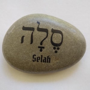 May include: A gray stone with the Hebrew word "Selah" written in black ink. The word "Selah" is also written in English below the Hebrew word.