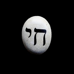 May include: A white stone with the Hebrew word "Chai" written in black paint.
