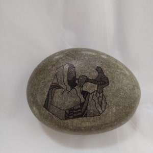 May include: A gray stone with a black and white image of a person playing a musical instrument. The person is wearing a long robe and a hat.