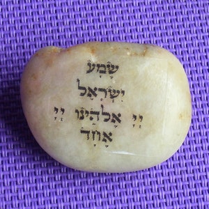 May include: A white stone with Hebrew writing on it. The writing says "Shema Yisrael Adonai Eloheinu Adonai Echad" which translates to "Hear O Israel, the Lord our God, the Lord is One."