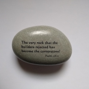May include: A gray stone with the text "The very rock that the builders rejected has become the cornerstone! Psalm 118:22" inscribed on it.
