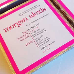 May include: Pink and gold glitter bat mitzvah invitation with the text "morgan alexis" in large, bold, pink letters. The invitation includes the date and time of the bat mitzvah service and party, as well as the location of both events.