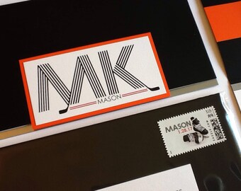 May include: A white card with black and red stripes forming the letters "MK" with the word "MASON" below. The card is on a black background.