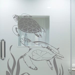 May include: A gray wall decal featuring two sea turtles swimming. The turtles are depicted in a detailed, stylized design, with one above the other. The decal includes aquatic plants at the bottom, creating a serene underwater scene.