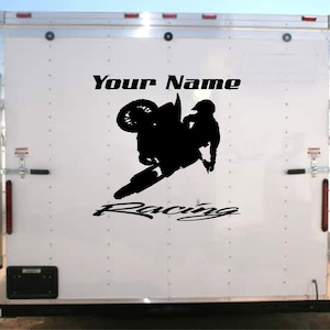May include: Black and white silhouette of a motocross rider jumping over a ramp with the text "Your Name Racing" on a white trailer.