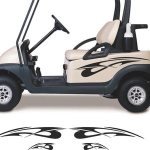 May include: A beige and dark gray golf cart with black decorative decals. The cart has a steering wheel, seats, and a roof. The wheels are silver. Additional black decals are at the bottom of the image.