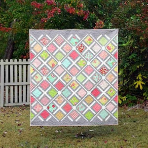 Puede incluir: Una colcha colorida con un patrón de diamantes en tonos de rosa, verde y amarillo. La colcha está colgada en un tendedero en un jardín.