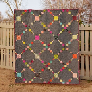 Puede incluir: Una colcha gris con un patrón de diamantes y cuadrados coloridos. La colcha está hecha con una variedad de telas, incluyendo estampados florales, lunares y rayas.