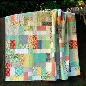 May include: A quilt pattern called "Grande Scrappy Tiles" by Meadow Mist Designs. The quilt is made of colourful fabric scraps in shades of red, green, blue, and yellow. The pattern is available in lap, twin, and queen sizes.