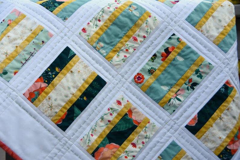 K&ouml;nnte beinhalten: Eine wei&szlig;e Steppdecke mit einem Rautenmuster. Die Steppdecke besteht aus verschiedenen Stoffen mit Blumen- und Streifenmustern in den Farben T&uuml;rkis, Gr&uuml;n, Gelb und Wei&szlig;.