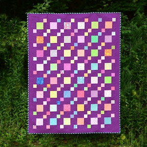 May include: A purple quilt with a diagonal pattern of colorful squares. The squares are in various shades of pink, yellow, blue, and green.
