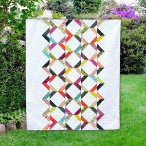 May include: A white quilt with a colourful geometric pattern of triangles and diamonds. The quilt is made with a variety of fabrics in shades of red, orange, yellow, green, blue, and purple.