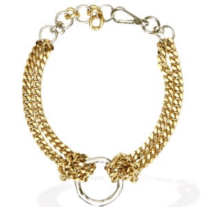 May include: Gold-tone chain bracelet with a silver-tone ring and clasp. The bracelet features two parallel chains connected by a silver-tone ring in the center. The chain is a curb style, and the clasp is a lobster claw style.