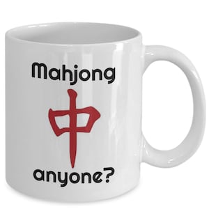 May include: White ceramic mug with the word "Mahjong" above a red Chinese symbol and the word "anyone?" below. The mug has a curved handle and is designed for hot beverages.