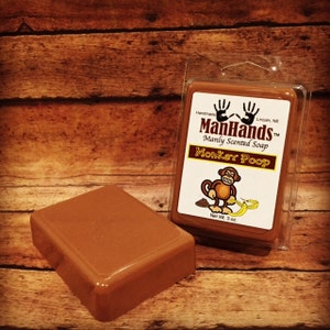 May include: A brown bar of soap in a clear plastic container. The label reads "ManHands™ Manly Scented Soap Monker Poop" with a cartoon monkey and banana. Net Wt. 3 oz.