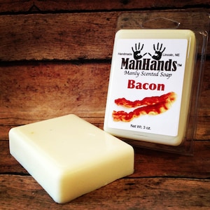 May include: A white bar of soap with a label that reads "ManHands™ Manly Scented Soap Bacon" and a picture of bacon. The soap is packaged in a clear plastic container. The soap weighs 3 ounces.