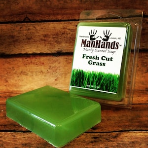 May include: A green bar of soap in a clear plastic package. The soap is labeled "ManHands™ Manly Scented Soap Fresh Cut Grass" and "Net Wt. 3 oz."