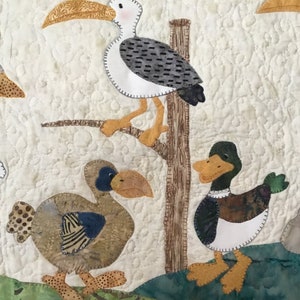 Puede incluir: Un tapiz de pared acolchado con p&aacute;jaros aplicados: una gaviota en una rama y dos patos. Las aves est&aacute;n hechas de telas estampadas en marr&oacute;n, azul, verde y blanco, sobre un fondo crema. El edred&oacute;n tiene un patr&oacute;n texturizado cosido.
