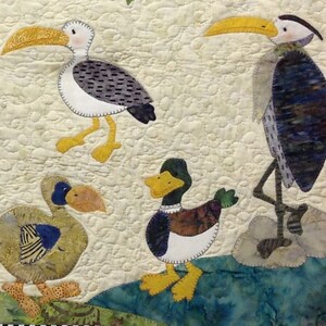 Puede incluir: Un textil acolchado con dise&ntilde;os caprichosos de aves. Las aves incluyen una gaviota, una garza y dos patos, cada uno con patrones de color y detalles &uacute;nicos. El fondo es de color beige claro con un patr&oacute;n acolchado, y las aves se colocan contra una escena de agua azul y verde.