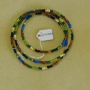 Può includere: Una collana di perline multifilo con perline marroni, verdi, blu, dorate e bianche. La collana ha un'etichetta attaccata che dice "Cernunnos".