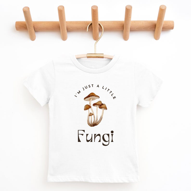 May include: White t-shirt with a brown mushroom graphic and the text "I'm just a little Fungi".