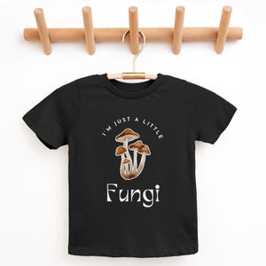 May include: Black t-shirt with a white graphic of mushrooms and the text "I'm just a little Fungi".